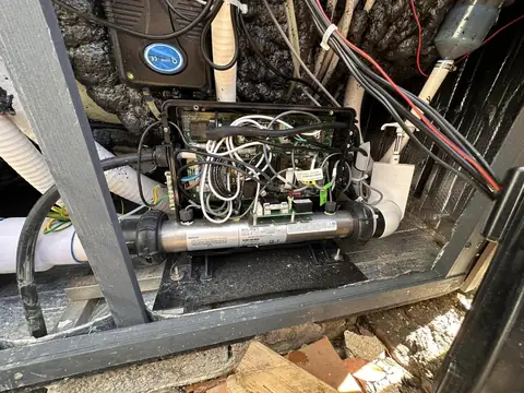 Hot tub control pack with its cover off, showing the circuit board, wiring and heater tube inside the cabinet