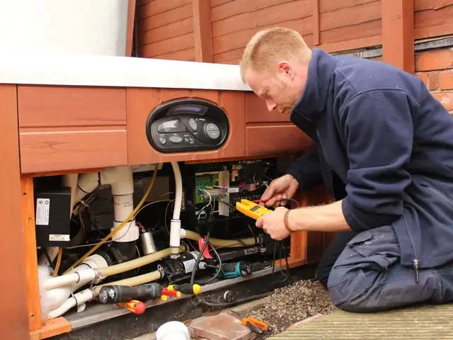 Jon Pennington testing a hot tub control pack with a clamp meter, the cabinet panel off and tools laid out