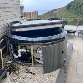 Round hot tub with its cabinet door open, showing the pump and pipework