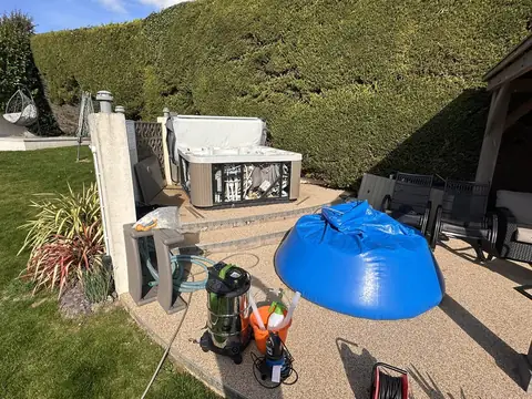 Our blue holding bag filled with water on a patio, beside a hot tub with its side panels off