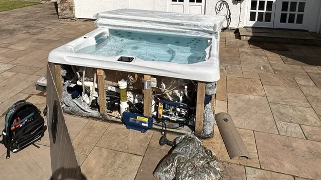 A hot tub on a patio in Falmouth with its side panels off, the equipment bay open and a tool bag beside it