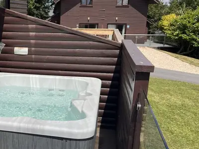 Hot tub with clear water on the deck of a timber holiday lodge, with other lodges and a lawn behind