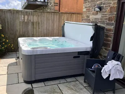 Grey hot tub with its cover folded back on a stone-flagged cottage patio, next to a garden chair with a towel on it