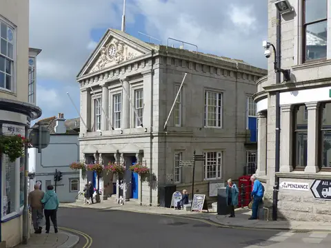 Helston Guildhall, a granite building with columns and a clock pediment, at the top of the main street