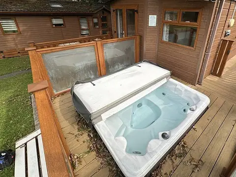A hot tub set into the deck of a timber holiday lodge, with its cover folded back