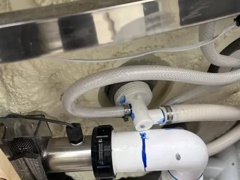 White pipework and joints under a hot tub, each joint marked with blue tape