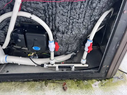Open hot tub cabinet showing pipework with red-handled valves, a control box and the sprayed foam insulation