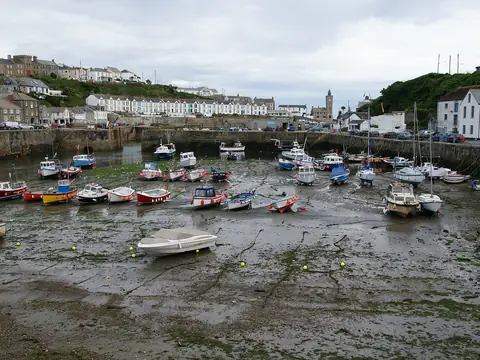 Porthleven harbour at low tide, with small boats on the sand and the clock tower beyond