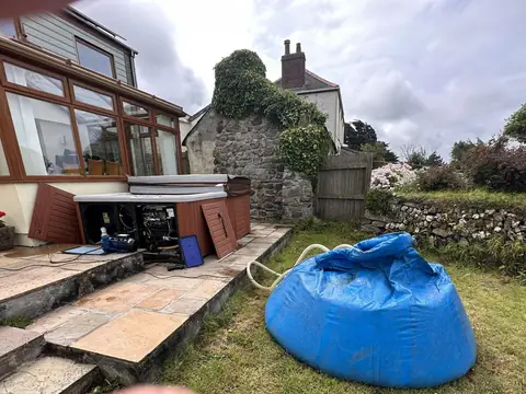 Our blue holding bag filled with a hot tub’s water on a lawn, beside the tub on a stone patio