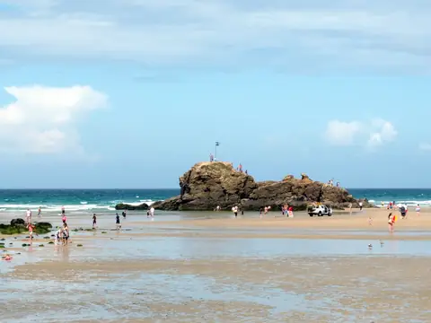 Chapel Rock on Perranporth beach at low tide, with people on the sand and the sea behind
