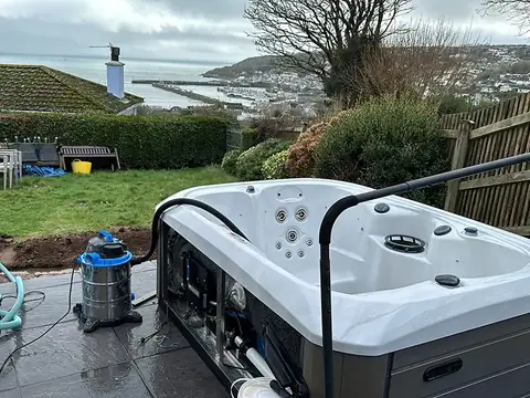 An emptied hot tub on a patio in Penzance with a wet vacuum beside it, and a view over the rooftops to the sea