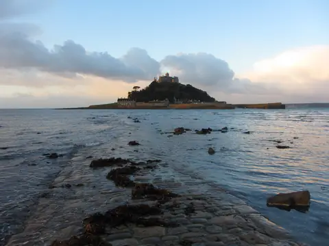 St Michael’s Mount seen from the rocky shore at Marazion, with the castle on the summit and clouds over Mount’s Bay