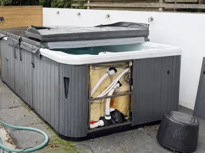 Grey hot tub with its cabinet panel off for a service, on a patio
