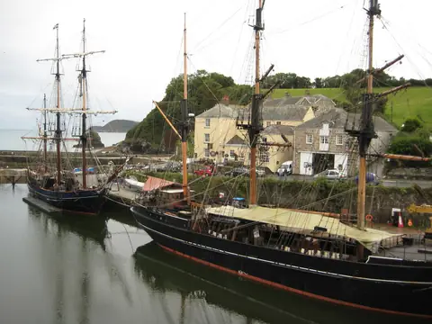 Tall ships moored in the inner harbour at Charlestown, with cottages around the quay