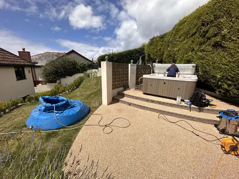 Our blue holding bag filled with water on a lawn beside a hot tub with its side panels off, near a set of garden steps