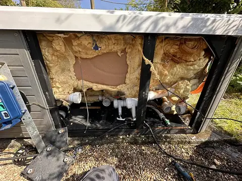 A hot tub with its side panels off, showing the foam insulation inside the cabinet and the pipework below
